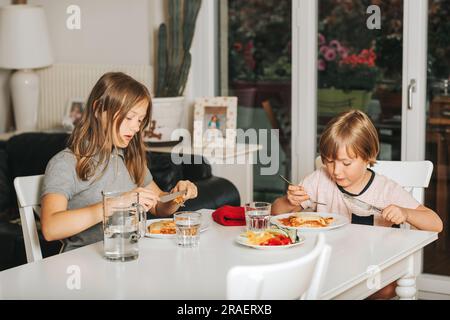 Due bambini che mangiano lasagne a pranzo, sano pasto fatto in casa per i bambini Foto Stock