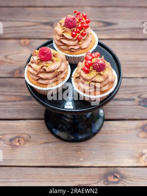 Cupcake al cioccolato con lampone fresco e ribes rosso su fondo di legno Foto Stock