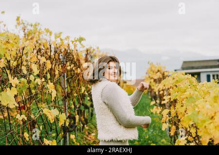 Ritratto autunnale di una giovane donna felice che si gode una bella giornata nei vigneti, indossando un pullover grigio e una morbida giacca bianca Foto Stock