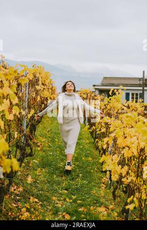 Ritratto autunnale di una giovane donna felice che si gode una bella giornata nei vigneti, indossando un abito a maglia grigia Foto Stock