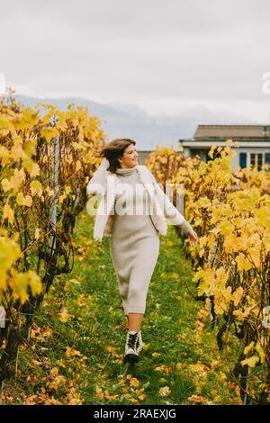 Ritratto autunnale di una giovane donna felice che si gode una bella giornata nei vigneti, indossando un abito a maglia grigia Foto Stock