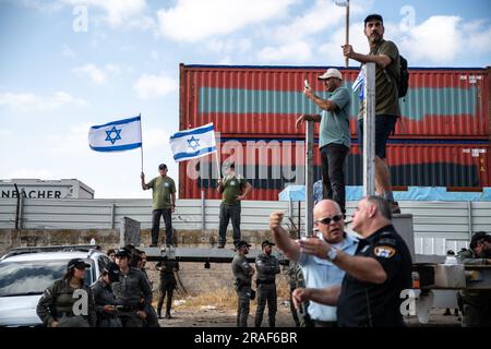 I manifestanti israeliani sventolano la bandiera israeliana accanto alla polizia israeliana e agli agenti di polizia di frontiera durante una manifestazione contro la revisione giudiziaria che blocca il cancello del porto di Haifa. Haifa, Israele. 3 luglio 2023. (Matan Golan / Sipa USA). Foto Stock