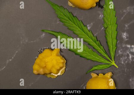 Un piccolo pezzo di frutta di burro di marijuana nella giornata calda su un tavolo nero di marmo con foglie fresche verdi Foto Stock