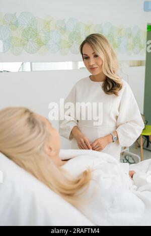 Vista posteriore verticale di una giovane donna irriconoscibile che si è consultata con una estetista seduta sul divano prima delle procedure facciali Foto Stock