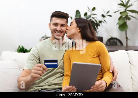 Felice moglie grata che bacia il suo marito sorridente, facendo shopping online Foto Stock
