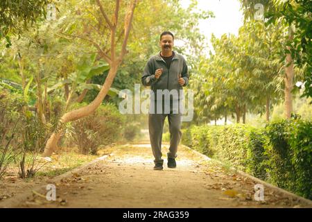 Buon indiano vecchio jogging nel parco su una pista da jogging e sentiero prendersi cura della sua salute Foto Stock