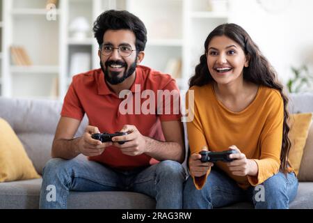 Giovane coppia indiana che gioca ai videogiochi con i joystick a casa Foto Stock