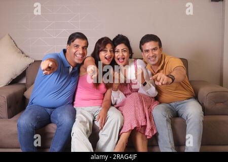 Amici indiani felici, coppie sedute su un divano, che si divertono a guardare la partita in tv e a celebrare i momenti vincenti. Foto Stock