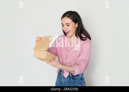 Un'emotiva e bella donna millenaria che apre una scatola di cartone Foto Stock