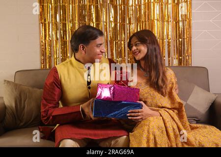 Un uomo indiano felice porta un bel regalo per sua moglie in sari. Entrambi indossano abiti etnici indiani su Diwali e celebrano il festival. Foto Stock