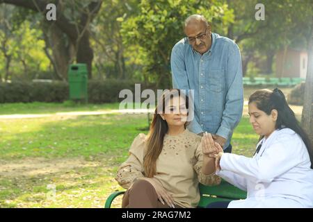 Medico che esamina i pazienti nel parco cittadino tra verdi seduti sulla panchina sotto l'albero. Foto Stock