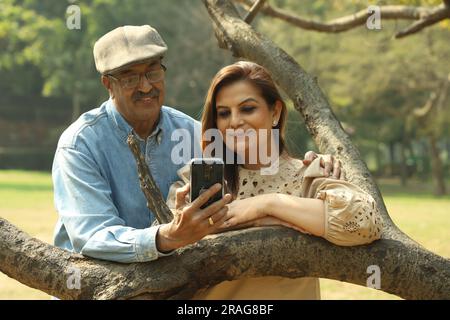 Una coppia indiana anziana si diverte a trascorrere una bella serata romantica nel parco verde. Stanno godendo, sorridendo e trascorrendo momenti di gioia. Foto Stock