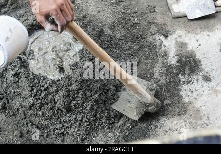 Lavoratore asiatico che utilizza zappa per miscelare la potenza del cemento con la sabbia Foto Stock