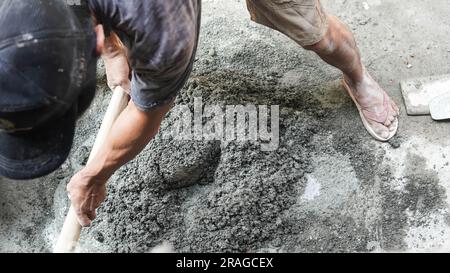 Lavoratore asiatico che utilizza zappa per miscelare la potenza del cemento con la sabbia Foto Stock