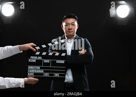 Attore asiatico che si esibisce mentre la seconda telecamera assistente tiene clapperboard sul palco. Industria cinematografica Foto Stock