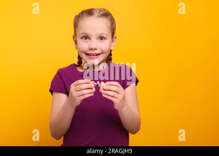 Ragazza carina che tiene un gustoso biscotto della fortuna con previsione su sfondo arancione Foto Stock
