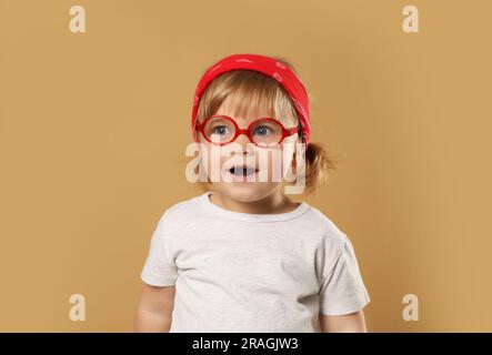 Graziosa bambina con gli occhiali su sfondo marrone chiaro Foto Stock