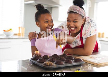 Felici madre e figlia afroamericana che decorano i cupcake in cucina Foto Stock