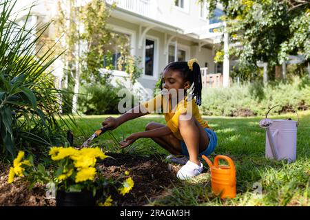 Ragazza afro-americana che scava sporco con gli attrezzi su terreni erbosi in cortile fuori casa Foto Stock