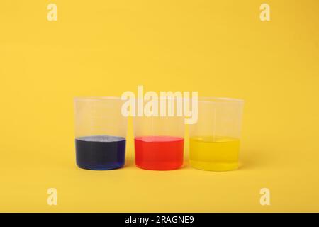 Becher con liquidi colorati su sfondo giallo. Set di esperimenti chimici per bambini Foto Stock