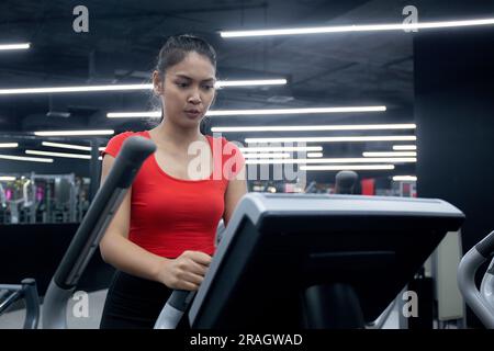 Ritratto giovane donna asiatica che cammina sul tapis roulant in palestra fitness, esercizio cardio, sport e allenamento, salute e benessere, donna fare sfida con Foto Stock
