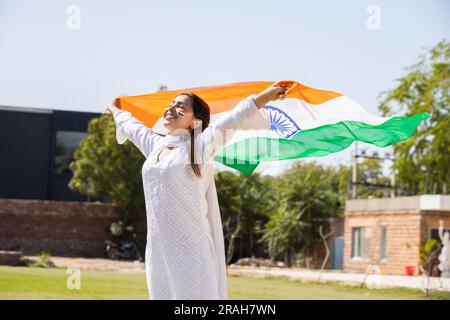 Giovane donna felice che indossa un tradizionale abito bianco che tesse bandiera indiana all'aperto nel parco, festeggia il giorno dell'indipendenza o la giornata della Repubblica. Foto Stock