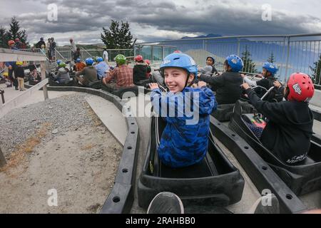 Una ragazza adolescente sorride con gioia sulla famosa attrazione turistica Skyline Luge sopra Queenstown e sul lago Wakatipu a South Island, nuova Zelanda. Ragazza in blu è stata rilasciata la modella. Foto: Rob Watkins Foto Stock