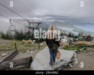 Una donna si erge sopra la famosa attrazione turistica Skyline Luge sopra Queenstown e il lago Wakatipu a South Island, nuova Zelanda. La donna che ammira la vista in primo piano viene rilasciata. Foto: Rob Watkins Foto Stock