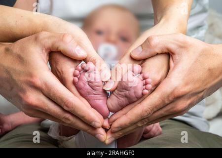 Dolce famiglia neonato che forma i piedi del bambino cuore i piedi del bambino nelle mani di mamma e papà genitore colore selettivo. Foto Stock