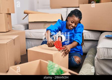 Donna afroamericana sorridente sicuro imballaggio scatola di cartone in nuova casa Foto Stock
