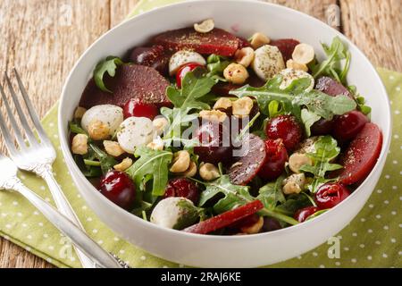 Insalata vegetariana di rucola, barbabietole, ciliegie mature, formaggio, nocciole da vicino in una ciotola sul tavolo. Orizzontale Foto Stock