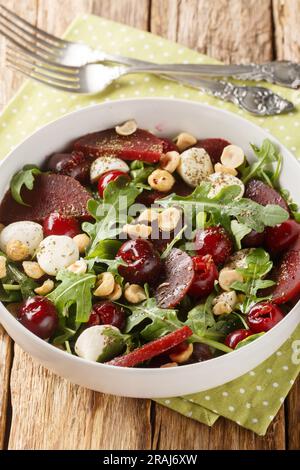 Insalata estiva fresca di rucola, barbabietole al forno, ciliegie, mozzarella, nocciole da vicino in una ciotola sul tavolo. Verticale Foto Stock