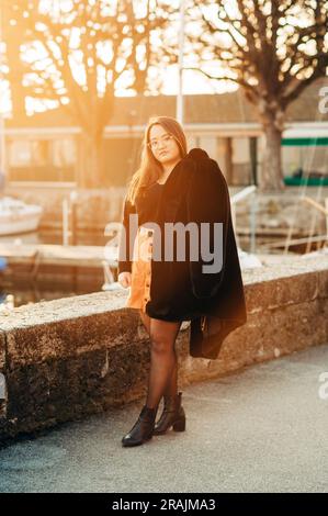 Ritratto all'aperto di un modello asiatico più grande, con un cappotto nero in pelliccia sintetica, in posa accanto al lago Foto Stock