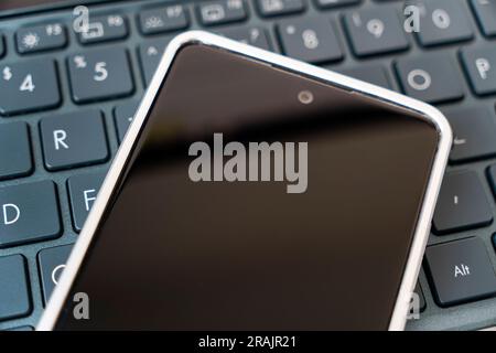 uno schermo vuoto su uno smartphone appoggiato su una tastiera nera di un laptop. vista dall'alto. Copia spazio Foto Stock
