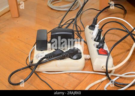 Cavi aggrovigliati sul pavimento in parquet. Pannelli elettrici sovraccaricati sul pavimento in legno. Cavi elettrici in disordine Foto Stock