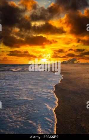 Onde di bianco schiuma di mare lavarsi su una spiaggia alla luce della sera. Foto Stock