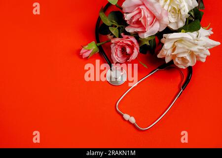 Mazzo di fiori di rosa e stetoscopio su sfondo rosso brillante. Giorno del Dottore nazionale. Buona giornata di infermiera. Vista superiore con spazio di copia Foto Stock