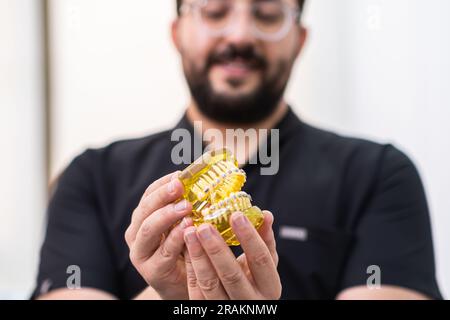 Ortodontista che mostra mascelle artificiali umane in plastica gialla con staffe metalliche installate Foto Stock