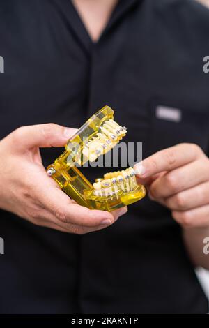 Medico in camicia nera con ganasce umane in plastica artificiale con bretelle in metallo che aiutano il paziente Foto Stock