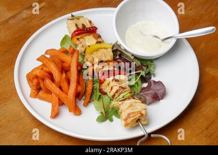 Souvlaki greco, patate dolci e salsa di yogurt tzatziki serviti sul piatto nel ristorante Foto Stock