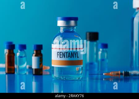 primo piano di un flaconcino simulato di fentanil su un tavolo blu accanto a una siringa e ad altre fiale diverse Foto Stock