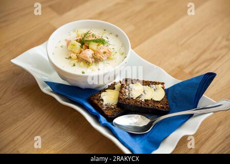Una ciotola di zuppa finlandese Lohikeitto servita su un tavolo di legno con un pezzo di pane di segale svedese. Brodo cremoso, patate teneri e salmone rosa friabile Foto Stock