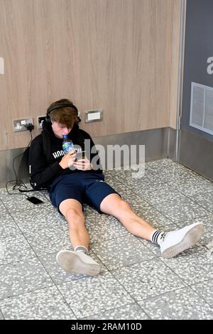 Seduto sul telefono di ricarica a pavimento collegato alla presa di alimentazione, Regno Unito Foto Stock