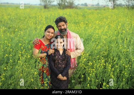 Una felice famiglia di agricoltori indiani che si trova in un campo di senape di giorno e gode di profitti agricoli. Sono felici di ottenere benefici dalle colture di senape. Foto Stock