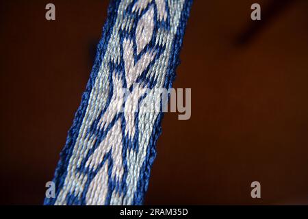 Primo piano di una cintura di seta bianca e blu fatta a mano prodotta dalla tessitura di tablet. Immagine orizzontale con messa a fuoco selettiva Foto Stock