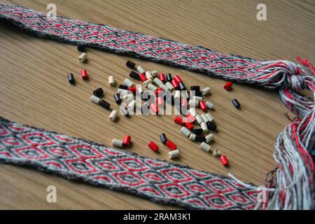 Primo piano di una cintura fatta a mano prodotta dalla tessitura di compresse e di alcune perle marroni, beige e rosse. Immagine orizzontale con messa a fuoco selettiva Foto Stock