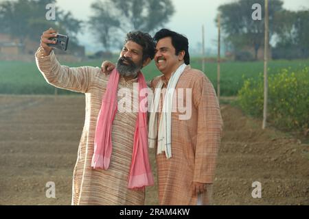 Bella composizione di due contadini indiani in piedi nel campo. Concetto agricolo che ritrae gli agricoltori al lavoro guardando lo smartphone. Foto Stock