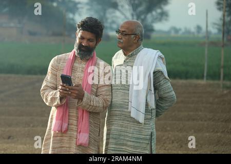 Bella composizione di due contadini indiani in piedi nel campo. Concetto agricolo che ritrae gli agricoltori al lavoro guardando lo smartphone. Foto Stock