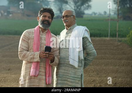 Bella composizione di due contadini indiani in piedi nel campo. Concetto agricolo che ritrae gli agricoltori al lavoro guardando lo smartphone. Foto Stock