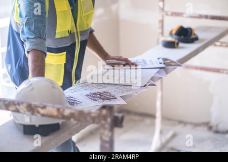 Lavoratore che controlla i documenti dei progetti di ristrutturazione che si trovano sulle attrezzature per l'edilizia Foto Stock